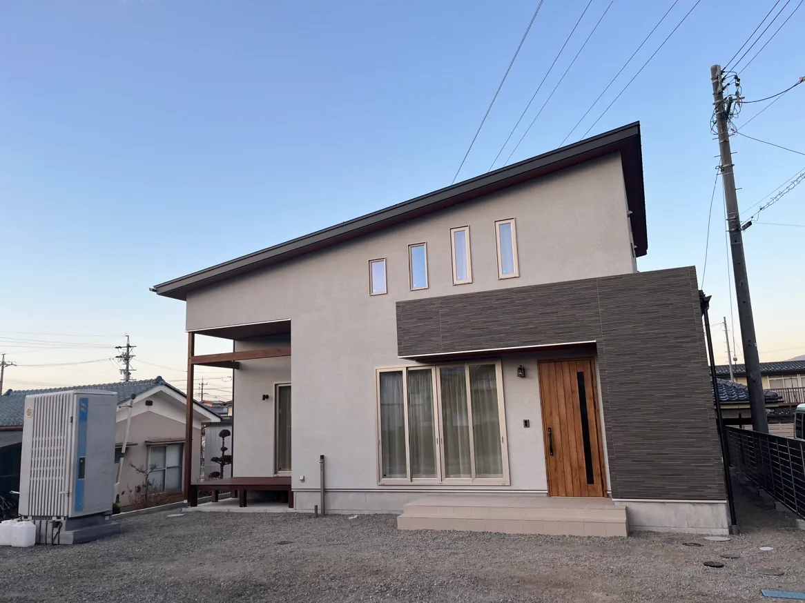 片流れ屋根と石貼り風アクセント壁が映えるモダンな外観。木目調の玄関ドアとウッドデッキ